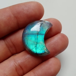 Peut inclure: Un cabochon de labradorite en forme de croissant de lune. La pierre a un éclat iridescent bleu-vert.