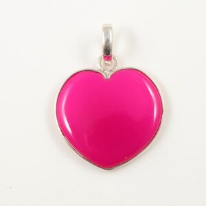 May include: A silver heart-shaped pendant with a bright pink gemstone.
