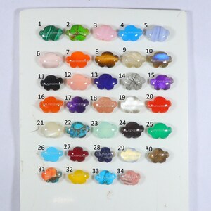 Peut inclure: Une collection de 34 cabochons de pierres précieuses de différentes couleurs en forme de nuage. Les cabochons sont disposés en rangées sur une carte blanche avec les numéros 1 à 34 imprimés à côté de chaque pierre.