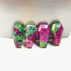 May include: Four green and pink gemstone cabochons in a coffin shape. The gemstones are polished and have a smooth surface.