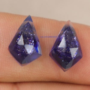 Peut inclure: Deux pendentifs en pierre précieuse bleue de forme en goutte facetée. Les pendentifs ont une finition scintillante et brillante et présentent un motif triangulaire blanc.