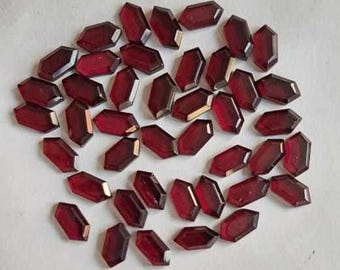 May include: A collection of faceted, dark red gemstones with a hexagonal shape. The gemstones are scattered on a white surface, showcasing their polished surfaces and rich color. These could be used for jewelry making or other crafts.