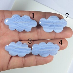 Könnte beinhalten: Vier blaue Achat-Cabochons in Wolkenform, jeder mit einem anderen Muster aus weißen und blauen Bändern. Die Cabochons sind von 1 bis 4 nummeriert.