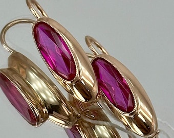 May include: A pair of gold earrings with pink oval-shaped gemstones. The earrings have a simple design and are perfect for everyday wear.