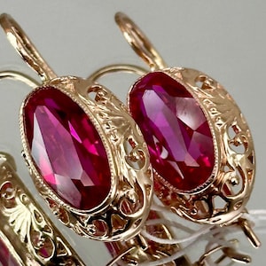 May include: A pair of gold earrings with oval-shaped red gemstones set in a delicate filigree design.