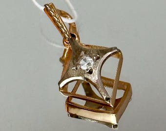 May include: A gold pendant with a diamond-shaped design and a small clear stone in the centre.