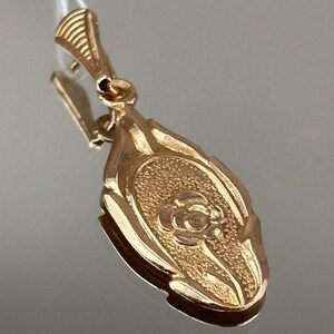 May include: A gold pendant with a detailed floral design. The pendant is oval shaped and has a textured surface.