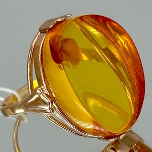May include: A gold ring with a large oval amber stone. The amber is a light yellow color and has a clear, translucent appearance.