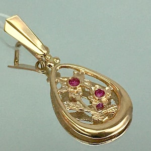 May include: A gold pendant with a delicate, openwork design featuring three red gemstones. The pendant is shaped like a teardrop and has a loop at the top for attaching to a chain.