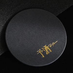 May include: A round, black coaster with a textured surface. Gold text in a stylized font is printed on the coaster. The text includes Chinese characters and the word "Boutique".