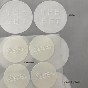 Puede incluir: Pegatinas circulares blancas y blanquecinas. Las pegatinas blancas tienen el texto "THE SET" en relieve. Las pegatinas blanquecinas tienen el nombre "Biaffka" en relieve. Tambi&eacute;n es visible el texto "Sticker Colors".