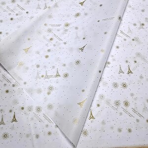 Może przedstawiać: Biały papier jedwabny z powtarzającym się wzorem złotych wież Eiffla i gwiazd. Na papierze nadrukowany jest tekst "FASHION CLASSIC".