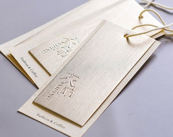 May include: Three gold-colored paper tags with a textured surface. Each tag has a string attached and features the text "unique" and a stylized Chinese character in raised lettering. The text "Fashion & Coffee" is printed on the bottom of each tag.