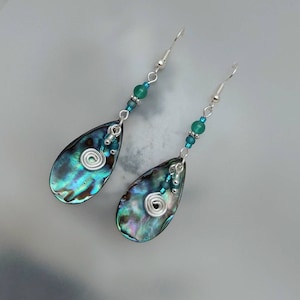 May include: A pair of teardrop-shaped earrings with iridescent abalone shell accents, silver wire spirals, and teal blue glass beads.
