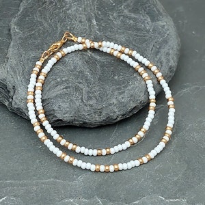 Peut inclure: Un collier d&eacute;licat en cha&icirc;ne dor&eacute;e avec des perles blanches. Le collier est superpos&eacute; et a un design simple.