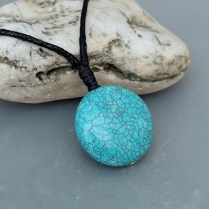 May include: A turquoise blue pendant with a cracked pattern hangs from a black cord necklace.