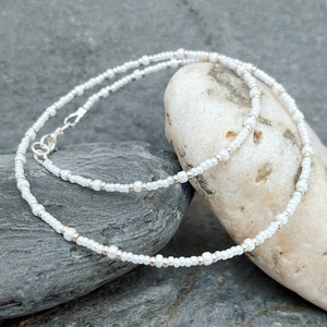 May include: A delicate white beaded necklace with a silver clasp. The necklace is made of small, round beads and is perfect for layering.