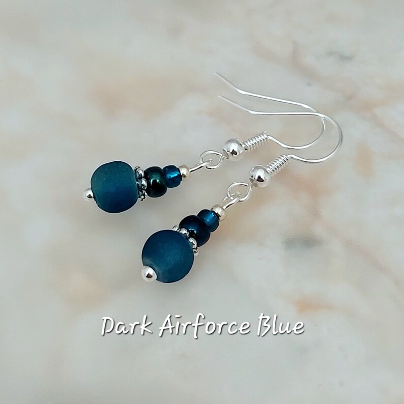 May include: A pair of silver dangle earrings with dark blue glass beads and silver beads. The earrings are labelled "Dark Airforce Blue".