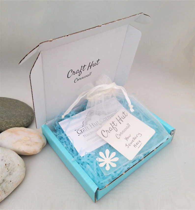 May include: A turquoise blue box with a white label that says "Craft Hut Cornwall" and a white tag that says "Your Jewellery Here". The box is filled with blue tissue paper and a white organza bag.
