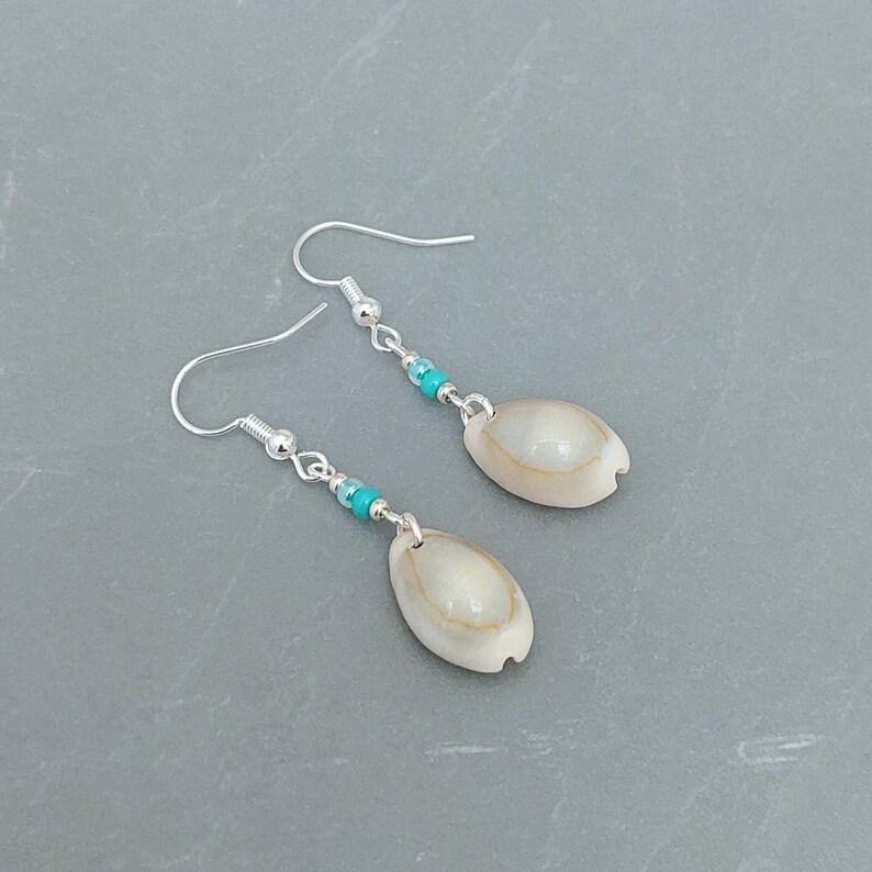 May include: A pair of silver earrings with turquoise beads and a white shell pendant.