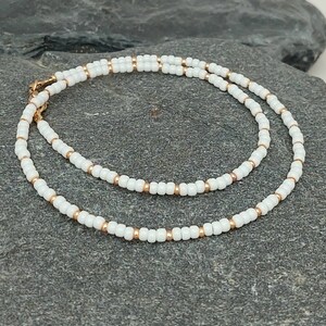 Peut inclure: Un collier d&eacute;licat en perles blanches et dor&eacute;es. Le collier est compos&eacute; de petites perles rondes enfil&eacute;es sur une fine cha&icirc;ne dor&eacute;e. Le collier est simple et &eacute;l&eacute;gant, et ferait un excellent cadeau pour toute occasion.