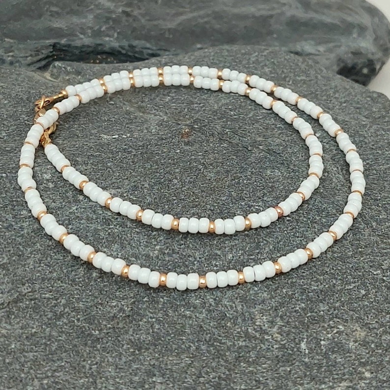 Peut inclure: Un collier d&eacute;licat en perles blanches et dor&eacute;es. Le collier est compos&eacute; de petites perles rondes enfil&eacute;es sur une fine cha&icirc;ne dor&eacute;e. Le collier est simple et &eacute;l&eacute;gant, et ferait un excellent cadeau pour toute occasion.