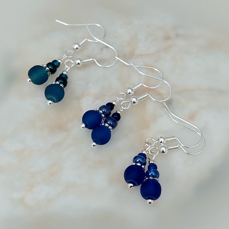 May include: A pair of silver dangle earrings with blue glass beads. The earrings have a simple design and are perfect for everyday wear.