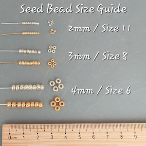 May include: A seed bead size guide featuring silver and gold beads arranged in rows and clusters. Text labels indicate 2mm/Size 11, 3mm/Size 8, and 4mm/Size 6. A wooden ruler at the bottom shows measurements in centimeters from 0 to 9 cm for scale.