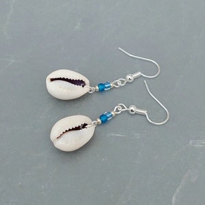 May include: A pair of silver earrings with white cowrie shells and blue glass beads.