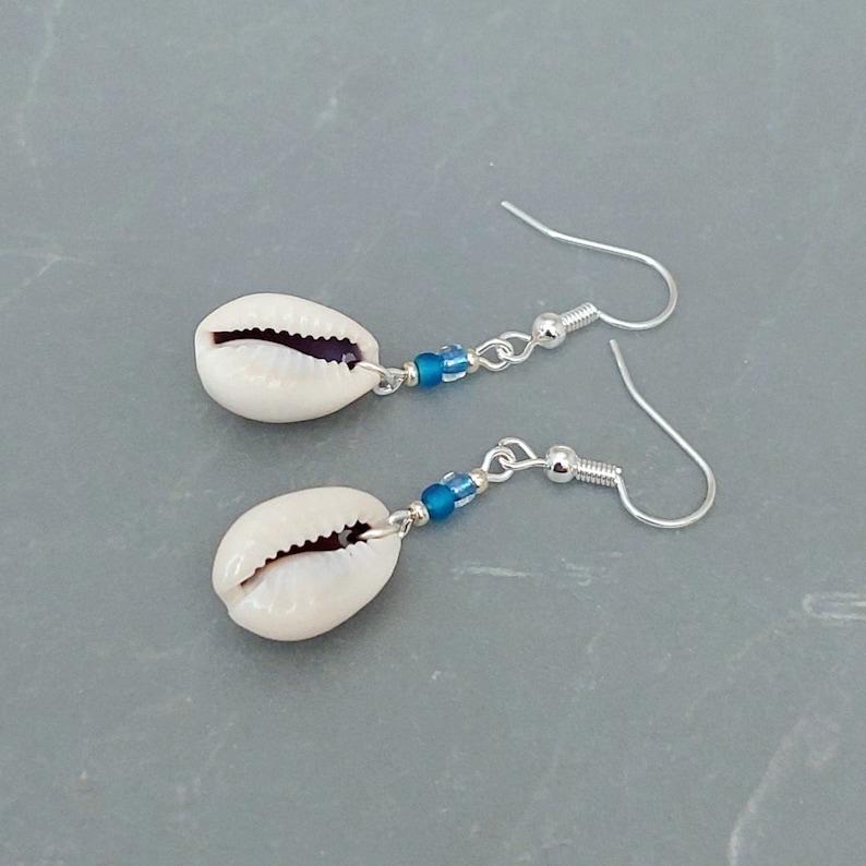 May include: A pair of silver earrings with white cowrie shells and blue glass beads.