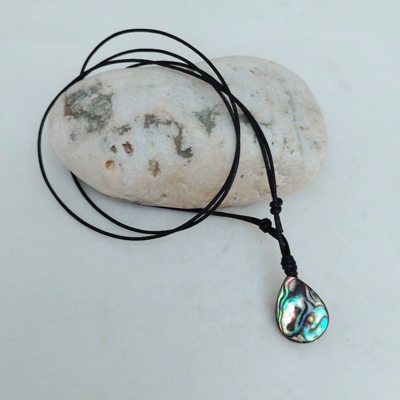 May include: A black cord necklace with a teardrop-shaped abalone shell pendant. The shell has iridescent green, blue, and brown colors.