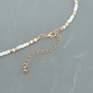 Peut inclure: Un collier de perles blanches avec un fermoir et une cha&icirc;ne d'extension dor&eacute;s. Le collier est compos&eacute; de petites perles rondes et pr&eacute;sente un design simple et &eacute;l&eacute;gant.