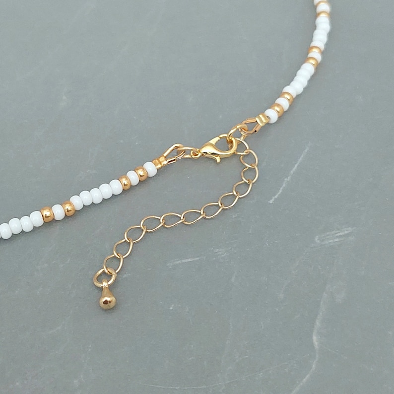Peut inclure: Un collier de perles blanches avec un fermoir et une cha&icirc;ne d'extension dor&eacute;s. Le collier est compos&eacute; de petites perles rondes et pr&eacute;sente un design simple et &eacute;l&eacute;gant.