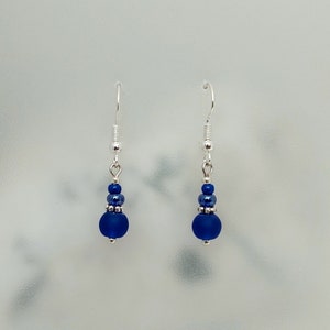 May include: A pair of silver dangle earrings with a dark blue glass bead and smaller silver beads.