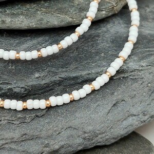 Peut inclure: Un collier de perles blanches et dor&eacute;es avec de petites perles rondes. Le collier est compos&eacute; de deux rangs de perles, un blanc et un dor&eacute;, qui sont entrelac&eacute;s.