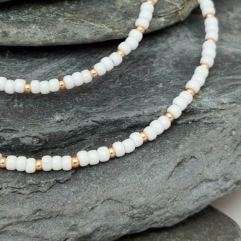 Peut inclure: Un collier de perles blanches et dor&eacute;es avec de petites perles rondes. Le collier est compos&eacute; de deux rangs de perles, un blanc et un dor&eacute;, qui sont entrelac&eacute;s.