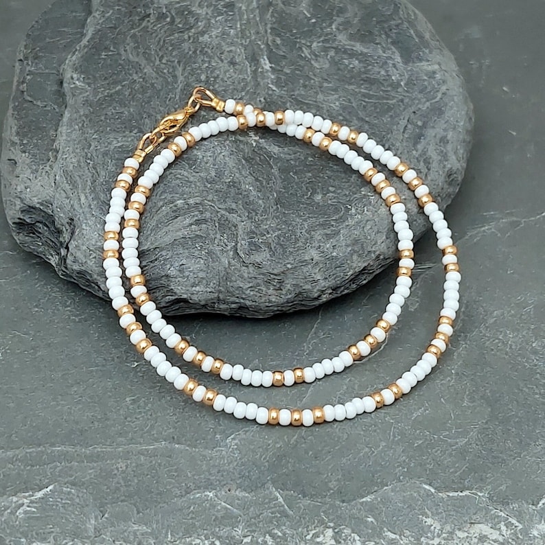Peut inclure: Un collier d&eacute;licat en cha&icirc;ne dor&eacute;e avec des perles blanches. Le collier est superpos&eacute; et a un design simple.