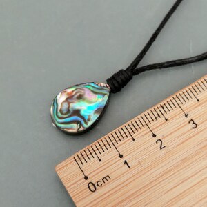May include: A teardrop-shaped iridescent abalone shell pendant on a black cord necklace. The pendant is approximately 1 inch long and is shown next to a ruler.