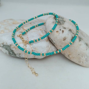 May include: A beaded anklet featuring alternating turquoise blue and metallic gold seed beads. The jewelry piece includes a gold-toned lobster claw clasp and an adjustable extender chain with a small round charm at the end of the chain.