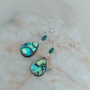 May include: A pair of silver dangle earrings with iridescent abalone shell teardrop pendants and green glass beads.