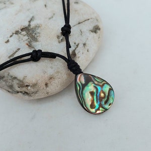 May include: A black cord necklace with a teardrop-shaped abalone shell pendant. The shell has iridescent green, blue, and brown colors.