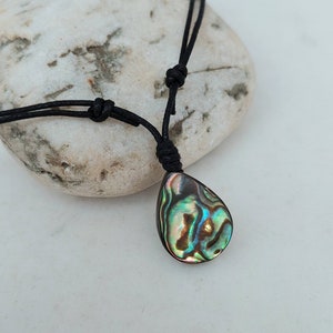 May include: A black cord necklace with a teardrop-shaped abalone shell pendant. The shell has iridescent green, blue, and gold colors.