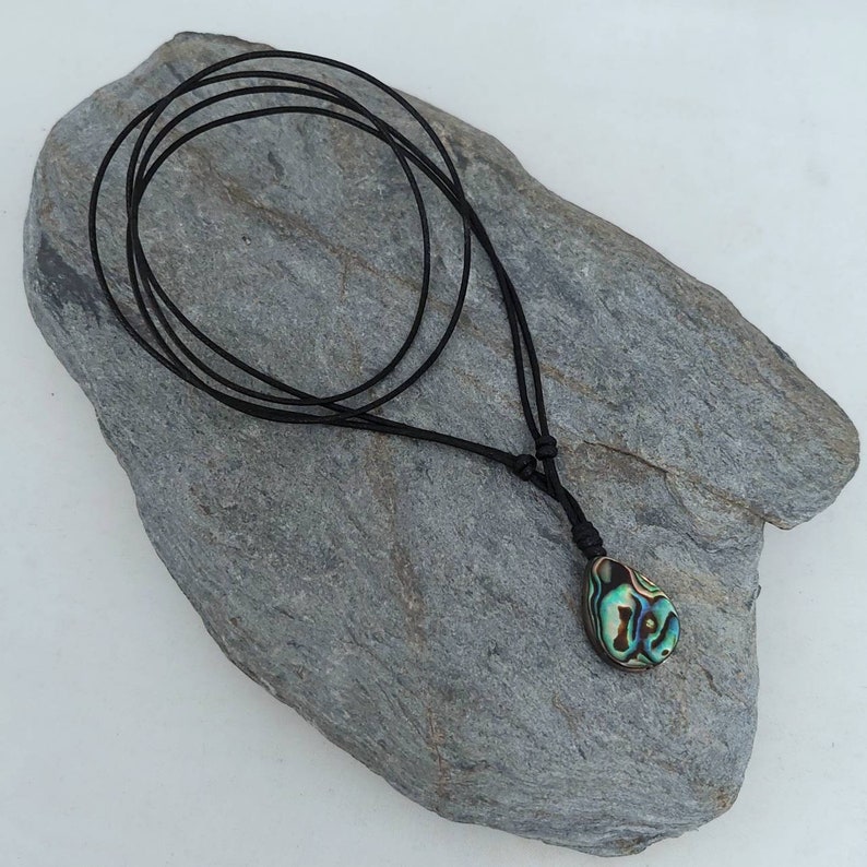 May include: A black leather cord necklace with a teardrop-shaped abalone shell pendant. The shell has iridescent green, blue, and gold colors.