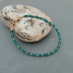 May include: A delicate bracelet made with small, iridescent green and gold beads. The bracelet has a gold clasp.