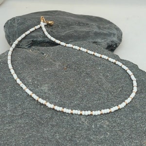 Peut inclure: Un collier d&eacute;licat en perles blanches avec des accents dor&eacute;s. Le collier est compos&eacute; de petites perles rondes et pr&eacute;sente un design simple et minimaliste.