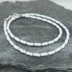Peut inclure: Un bracelet blanc en perles avec un fermoir argent&eacute;. Le bracelet est compos&eacute; de petites perles rondes et est superpos&eacute; sur lui-m&ecirc;me.