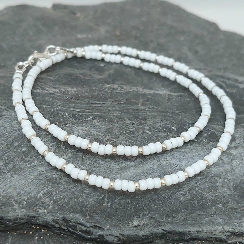 Peut inclure: Un bracelet blanc en perles avec un fermoir argent&eacute;. Le bracelet est compos&eacute; de petites perles rondes et est superpos&eacute; sur lui-m&ecirc;me.