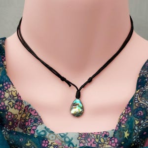 May include: A black cord necklace with a teardrop-shaped abalone shell pendant. The shell has iridescent blue, green, and gold colors.