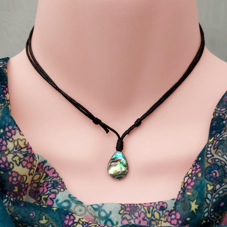 May include: A black cord necklace with a teardrop-shaped abalone shell pendant. The shell has iridescent blue, green, and gold colors.