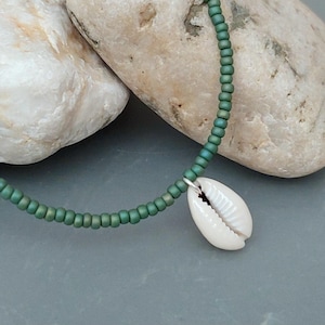May include: A green beaded necklace with a white seashell pendant. The necklace is on a grey background.